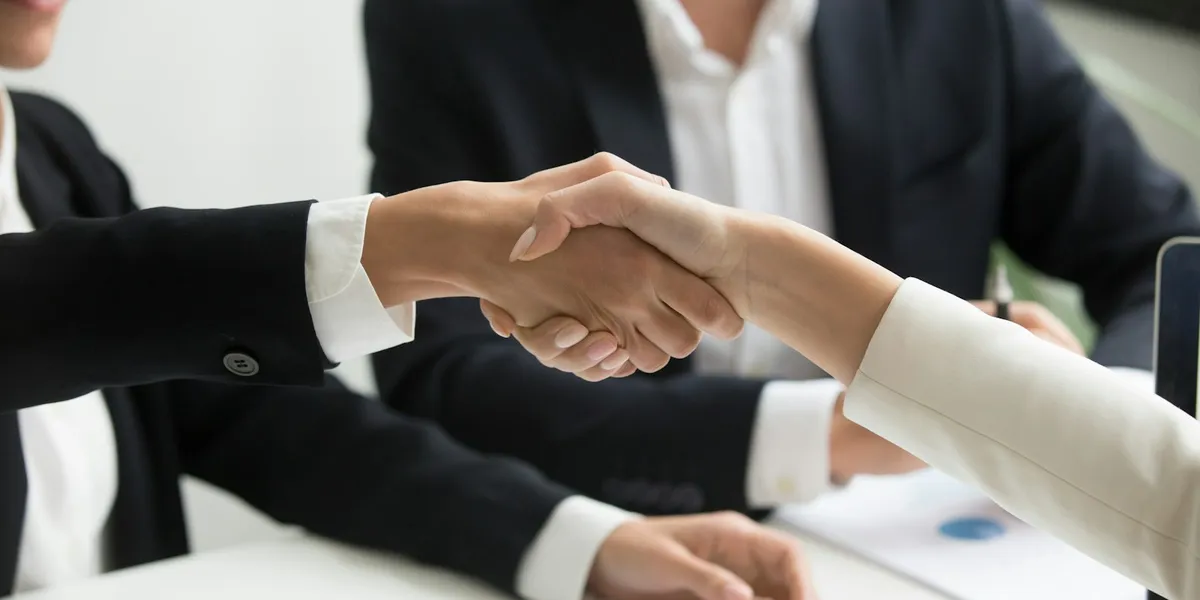 two people shaking hands in front of a laptop